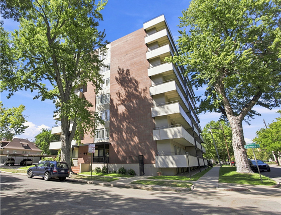 Charming brick apartment building with spacious balconies and lush greenery in a peaceful neighborhood setting.