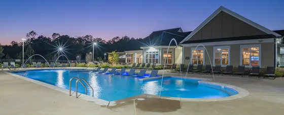Luxurious apartment complex with a stunning illuminated swimming pool and stylish lounging area at dusk.