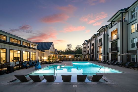 Luxurious apartment complex with a stunning illuminated swimming pool and stylish lounging area at dusk.