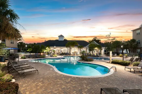 Luxurious apartment complex with a stunning illuminated swimming pool and stylish lounging area at dusk.