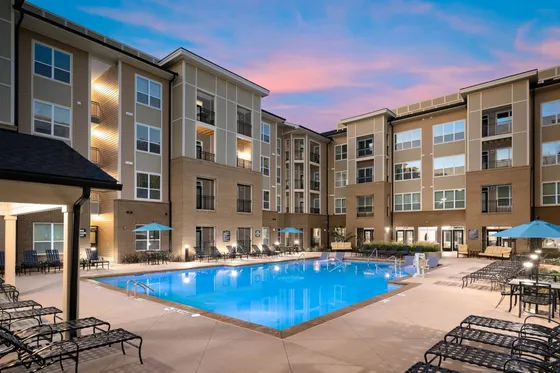 Luxurious apartment complex with a stunning illuminated swimming pool and stylish lounging area at dusk.