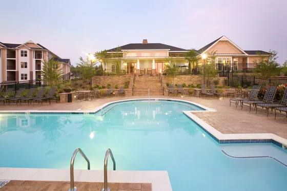 Luxurious apartment complex with a stunning illuminated swimming pool and stylish lounging area at dusk.