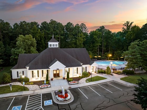 Charming community clubhouse with elegant architecture surrounded by lush greenery and a shimmering pool at sunset.