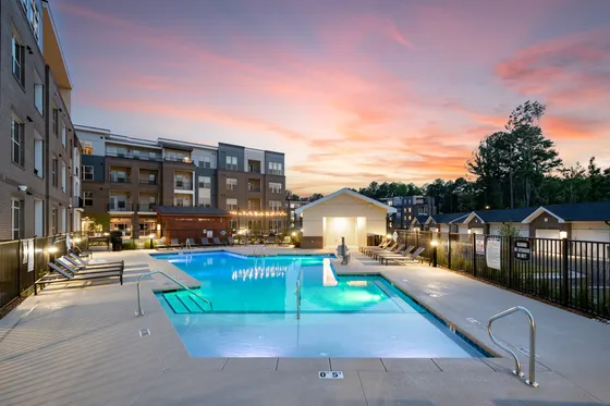 Luxurious apartment complex with a shimmering outdoor pool and modern amenities, set against a stunning sunset backdrop.