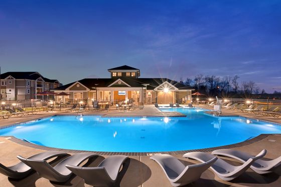 Luxurious apartment complex with a stunning illuminated swimming pool and stylish lounging area at dusk.
