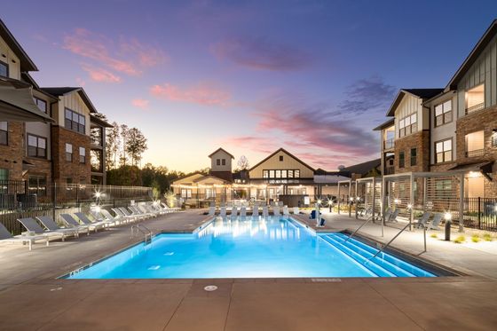 Dazzling apartment complex featuring a pristine outdoor pool with stylish poolside seating and charming evening ambiance.
