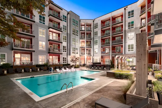 Modern apartment complex with a stunning outdoor pool area, surrounded by stylish multi-story buildings and lush greenery.