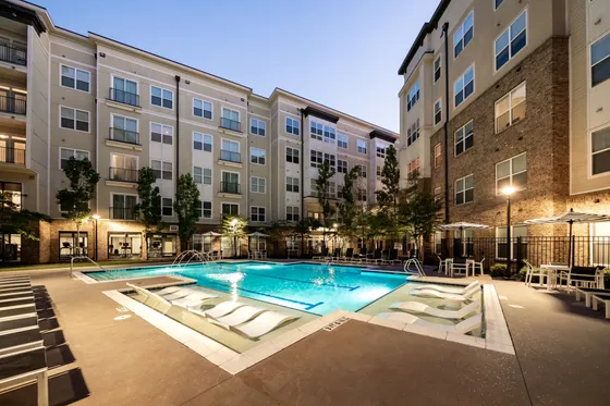 Elegant apartment complex with a luxurious outdoor pool area, surrounded by modern multi-story buildings at dusk.