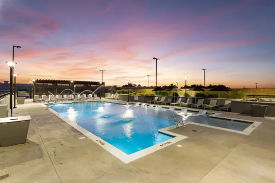 Luxurious rooftop pool area at sunset with elegant loungers and cascading water features, offering a serene urban escape.