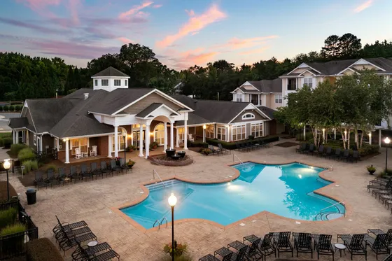 Charming apartment complex with an elegant clubhouse and an inviting outdoor pool, perfect for relaxation and social gatherings at sunset.