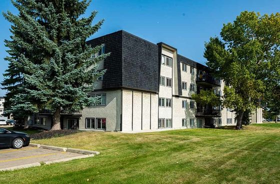 Exterior view of a Ascot Arms apartment building surrounded by lush greenery and trees, featuring a sleek design and spacious grounds.