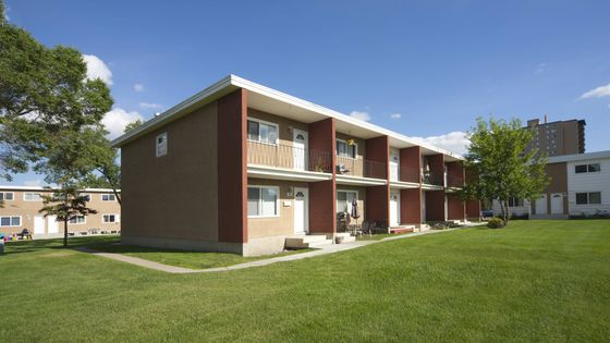 Charming two-story apartment building with private balconies, nestled in a lush green landscape under a clear blue sky.