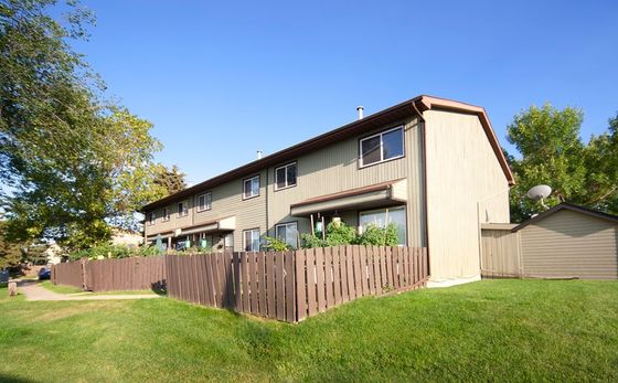 Charming multi-unit townhouse with a sunny exterior, beautiful green lawn, and private wooden fencing, nestled in a serene residential area.