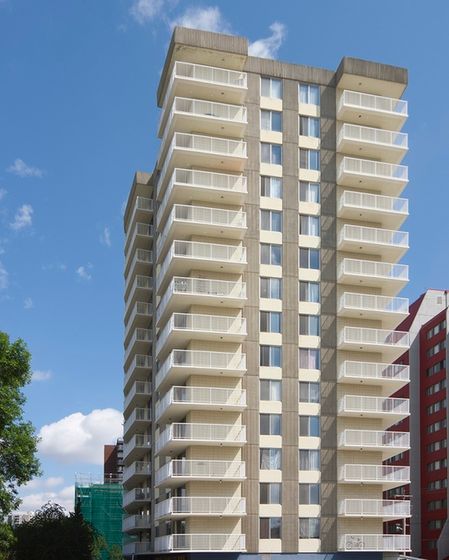 Modern high-rise apartment building with spacious balconies and panoramic city views against a clear blue sky.
