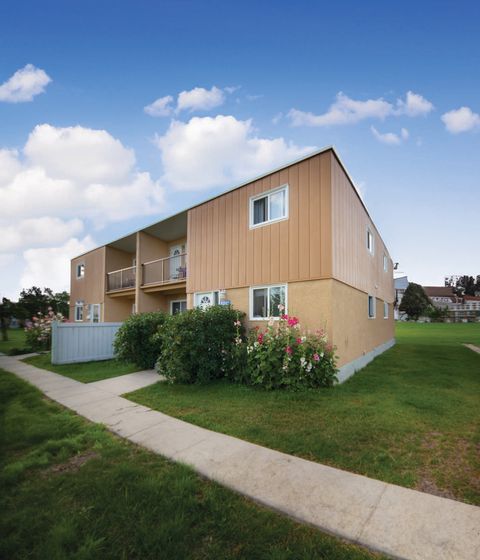 Charming apartment building exterior with manicured lawns, vibrant flower beds, and a clear blue sky, offering a serene and inviting atmosphere.