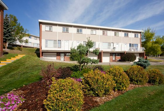 Charming multi-story apartment building surrounded by lush greenery and vibrant flower beds under a clear blue sky.
