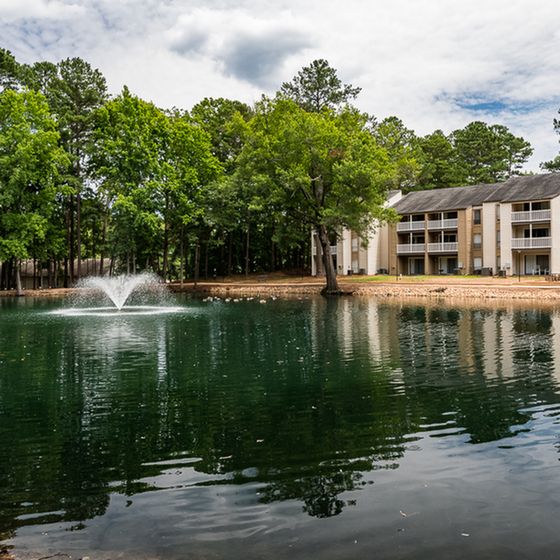 Serene apartment view with lush greenery, tranquil pond, and elegant fountain, offering a peaceful residential setting.