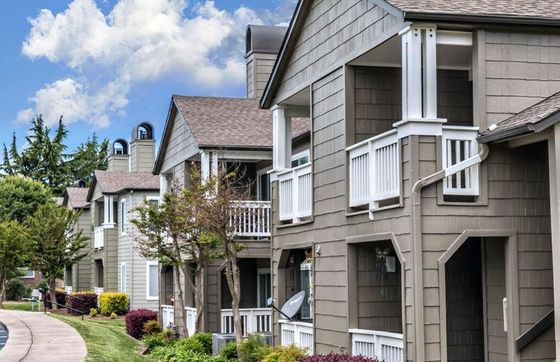 Charming suburban apartment complex with modern architecture, featuring private balconies and lush landscaping under a clear blue sky.
