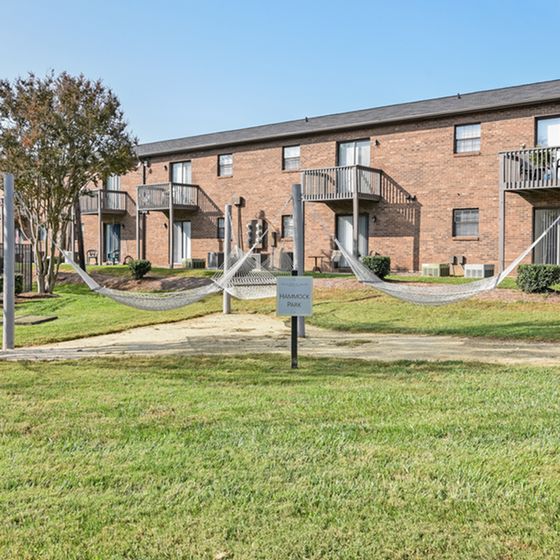 Charming apartment complex with brick exterior and private balconies, featuring a relaxing hammock park set amidst lush greenery.