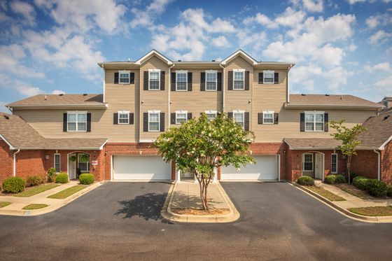 Charming townhouse facade with classic brick and siding design, featuring inviting green landscaping and spacious garages.