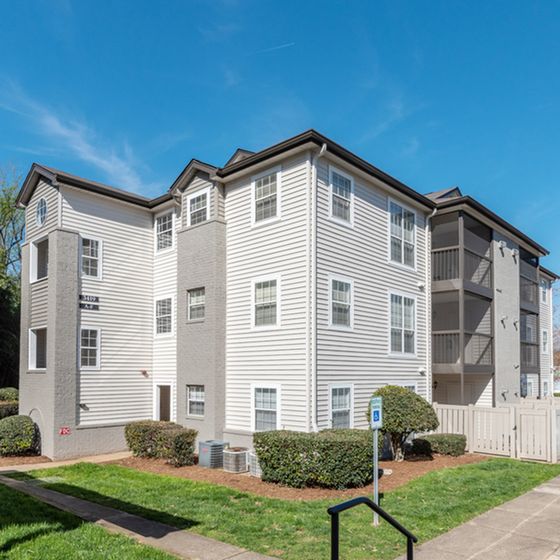 Charming multi-story apartment complex with modern siding, lush landscaping, and clear blue sky backdrop.