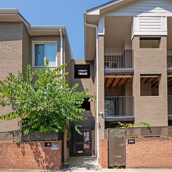 Charming modern apartment building with spacious balconies and inviting brick facade, surrounded by lush greenery.