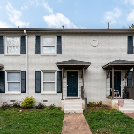 Charming townhouse exterior with white brick facade, navy shutters, and inviting entryway.