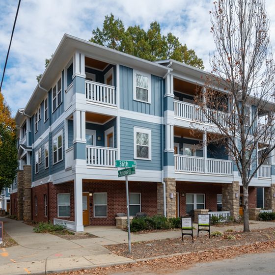 Charming three-story apartment building with elegant balconies and a brick facade, located on a peaceful tree-lined street.