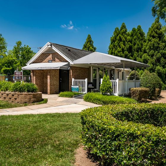 Charming brick property with a welcoming porch, surrounded by lush greenery and vibrant landscaping.
