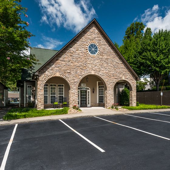 Charming stone exterior building with arched windows and inviting entrance, surrounded by lush greenery under a bright blue sky.