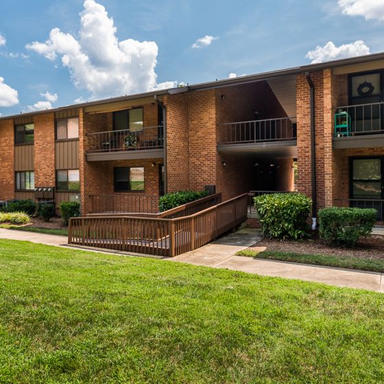 Charming brick apartment building with balconies overlooking well-manicured lawns on a sunny day.