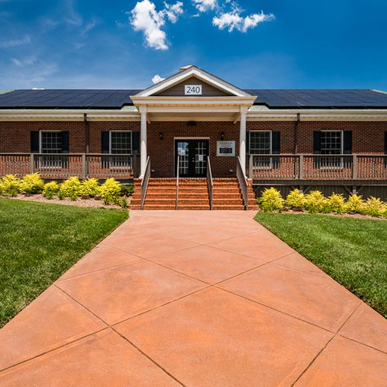 Charming brick building with welcoming entrance, vibrant landscaping, and solar-panelled roof against a sunny blue sky.