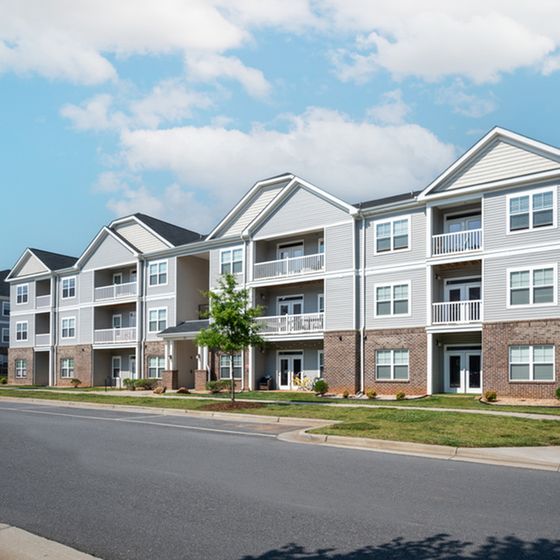 Modern apartment complex with elegant balconies and well-manicured lawns under a bright blue sky.