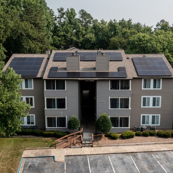 Modern apartment building with solar panels and lush greenery in a tranquil setting.
