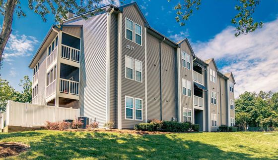 Charming modern apartment building with spacious balconies, surrounded by lush greenery and a clear blue sky.