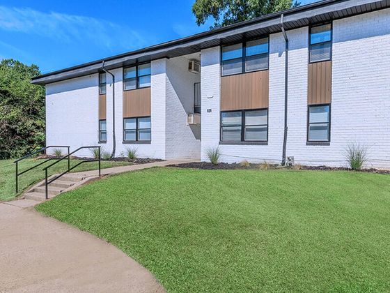 Charming apartment exterior with modern design and manicured green lawn, basking in natural sunlight.