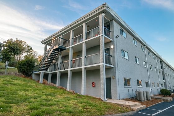 Charming three-story apartment building with classic design, featuring spacious balconies and lush green surroundings.