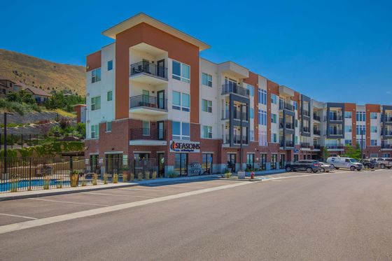 Modern apartment complex with vibrant exterior design, featuring balconies and spacious parking, set against a scenic hillside backdrop.
