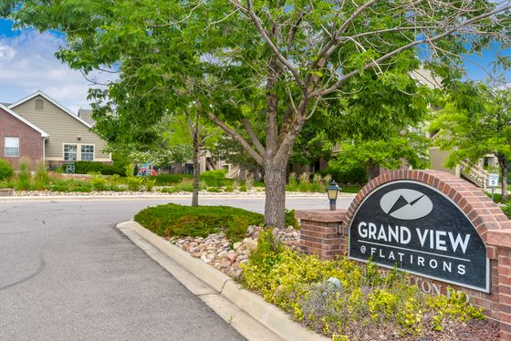 Charming entrance of Grand View at Flatirons, surrounded by lush greenery and well-maintained landscapes on a sunny day.