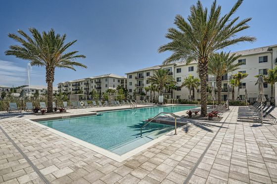 Elegant apartment complex with a luxurious outdoor pool surrounded by palm trees and lounge chairs, perfect for a relaxing retreat.