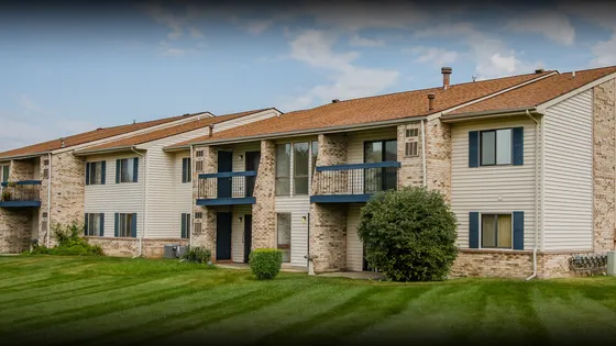 Charming apartment building with brick and siding exterior, featuring cozy balconies overlooking lush green lawns under a clear blue sky.