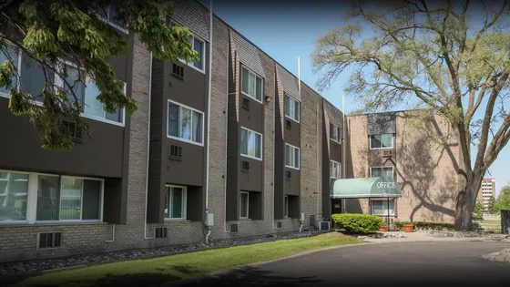 Modern apartment complex with elegant brick facade and lush green surroundings, featuring a welcoming office entrance.