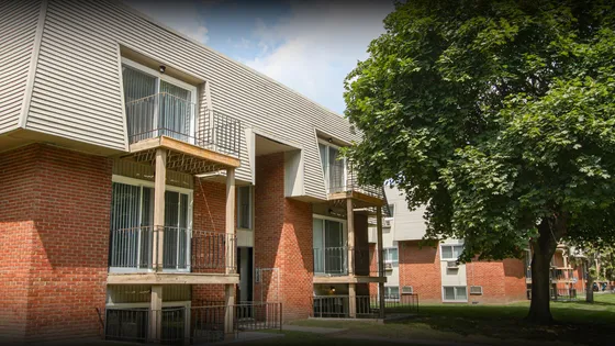 Charming apartment complex featuring modern balconies, red brick facade, and lush green surroundings, perfect for a tranquil living experience.