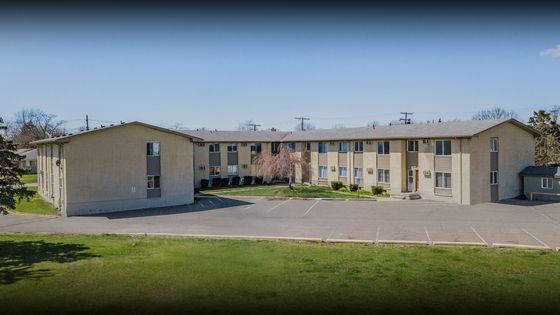 Inviting apartment complex with charming architecture, ample parking, and lush green surroundings on a sunny day.