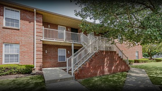 Charming red brick apartment exterior with white railings and lush green surroundings, offering a welcoming entrance and serene ambiance.