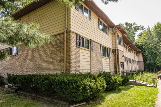 Charming brick apartment building with well-maintained landscaping and lush greenery, offering serene suburban living.