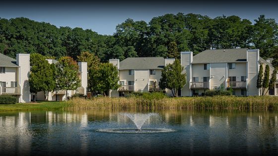 Charming lakeside apartment complex with elegant white buildings, surrounded by lush greenery and featuring a serene water fountain.