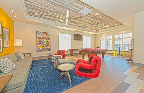 Chic lounge area with a modern design, featuring a pool table, unique red chairs, cozy gray sofas, and vibrant artwork on a textured ceiling background.