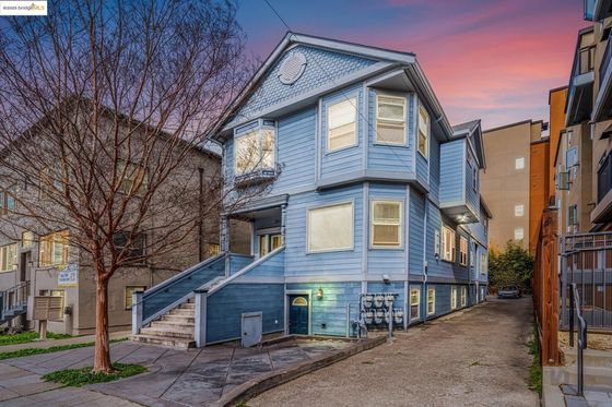 Charming two-story blue house with bay windows at sunset, featuring a welcoming staircase entrance and a quaint urban setting.