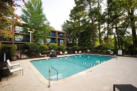 Serene apartment community showcasing a sparkling swimming pool surrounded by lush greenery and stylish sun loungers.